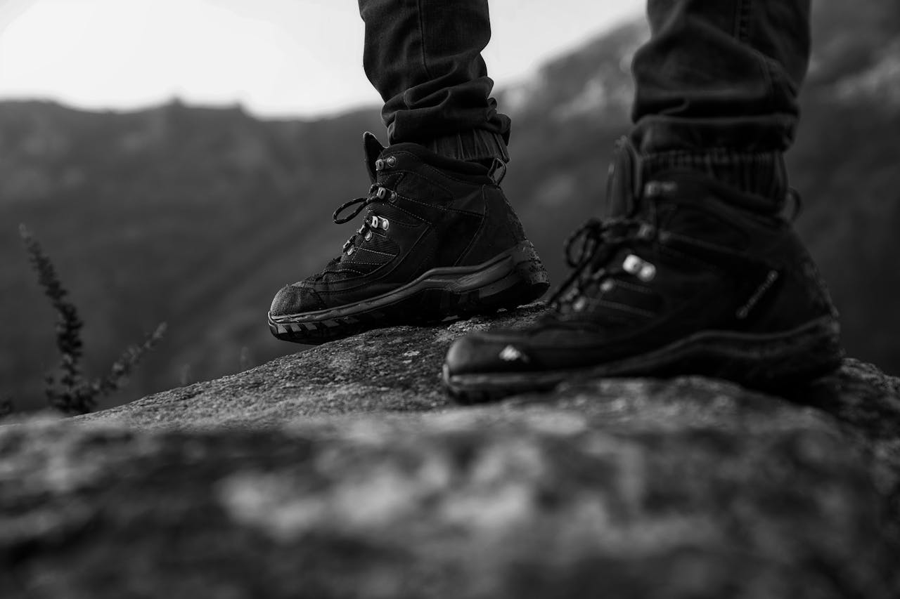 Close-up of hiking boots standing on a rock, showcasing outdoor adventure style in monochrome.