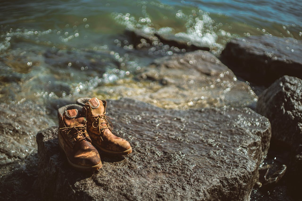 Abandoned hiking boots on a rocky shoreline with waves crashing in.